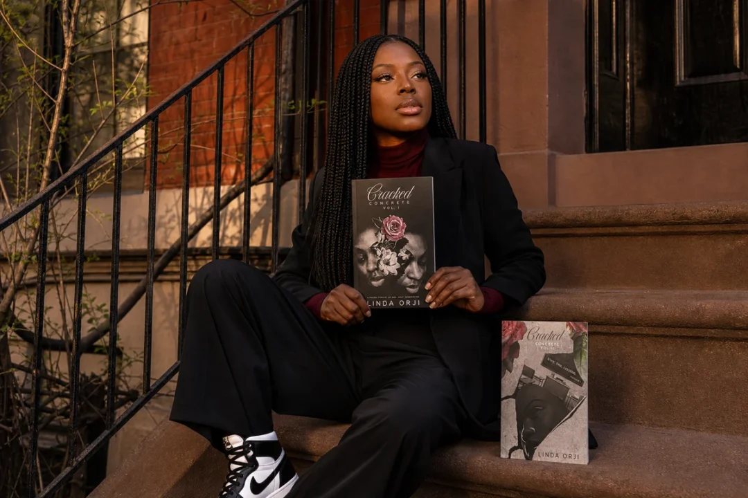 Linda Orji seated on a New York City brownstone stoop holding Cracked Concrete Volume I beside Volume II